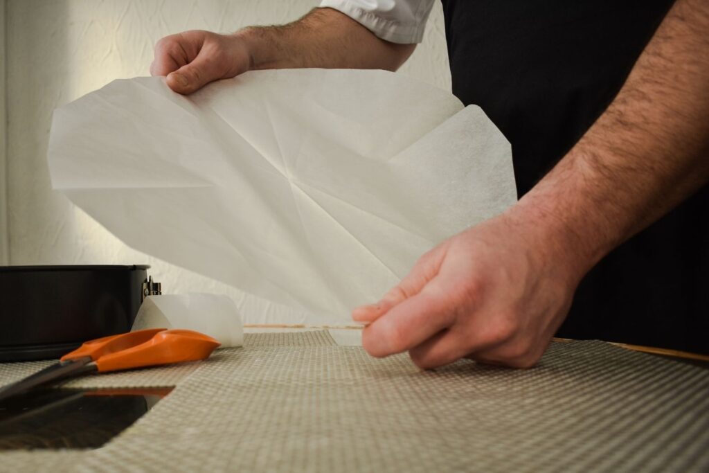 Las mejores alternativas al papel pergamino para hornear con masa fermentada: hombre que sostiene un trozo de papel pergamino en forma de círculo.  Hay unas tijeras naranjas a su lado.