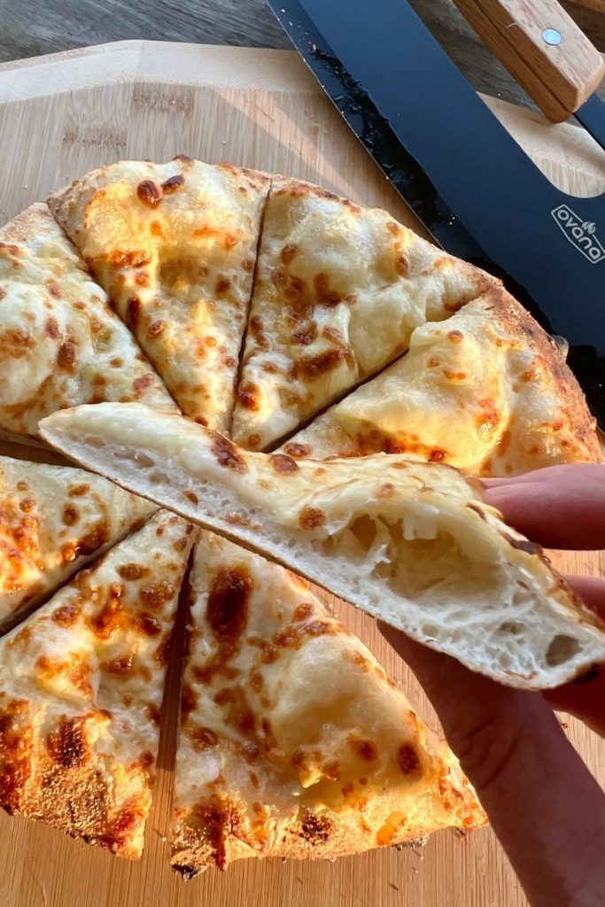 Foto que muestra una mano sosteniendo una rebanada de pizza para mostrar una corteza perfecta: no se hunde cuando se sostiene por los bordes.