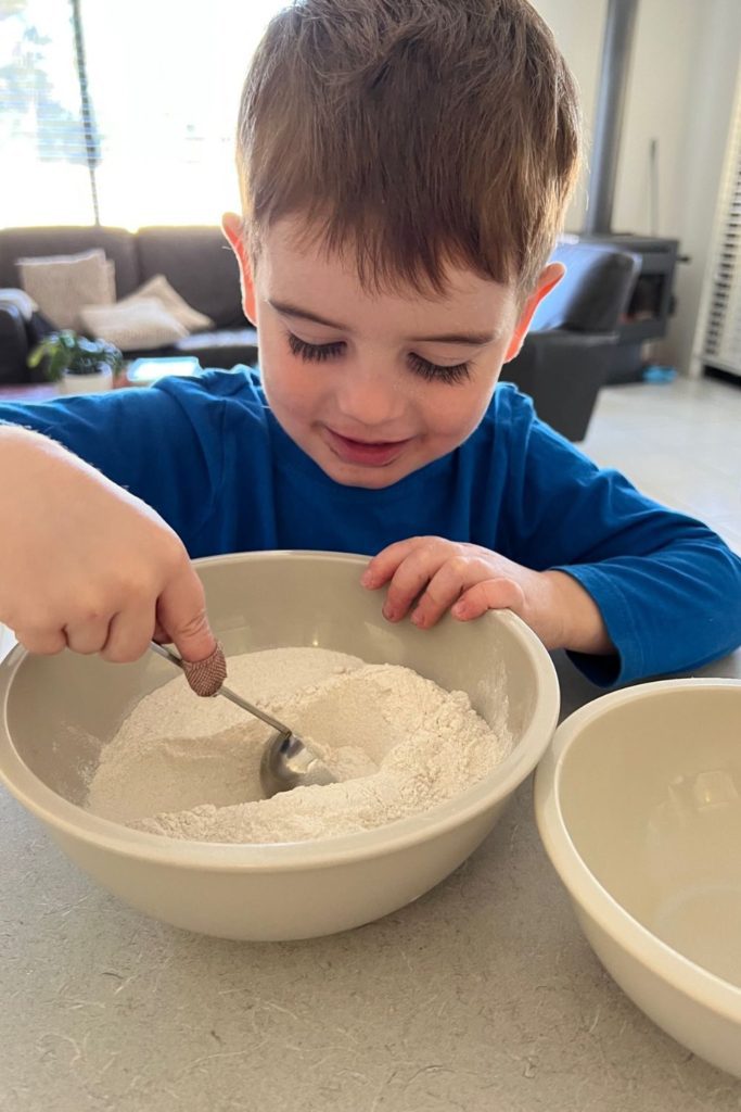 Niño pequeño sacando harina con una cuchara dosificadora.