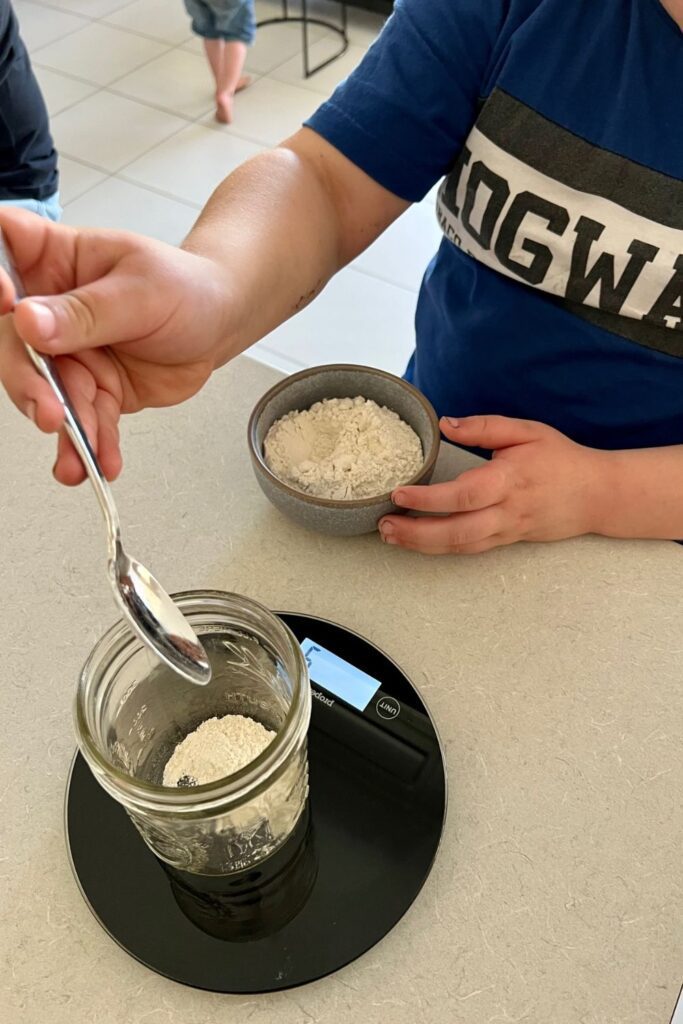 Niño pesando harina para crear un iniciador de masa fermentada: cómo enseñar a los niños a hornear pan de masa fermentada