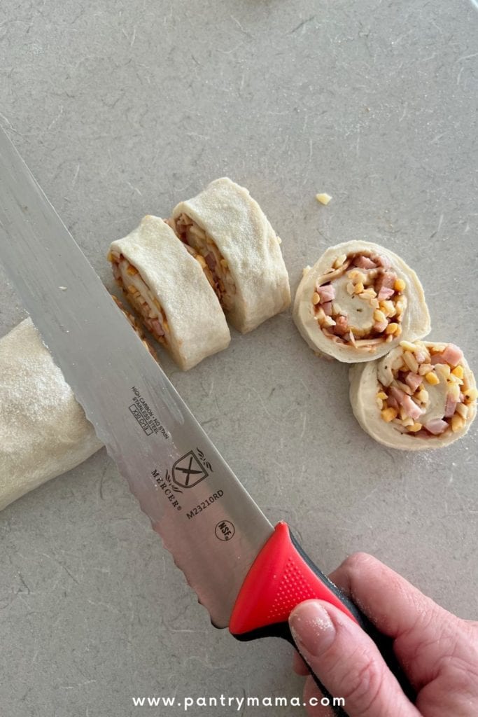 Usando un cuchillo de pan para medir y cortar los rollos de pizza al tamaño adecuado.