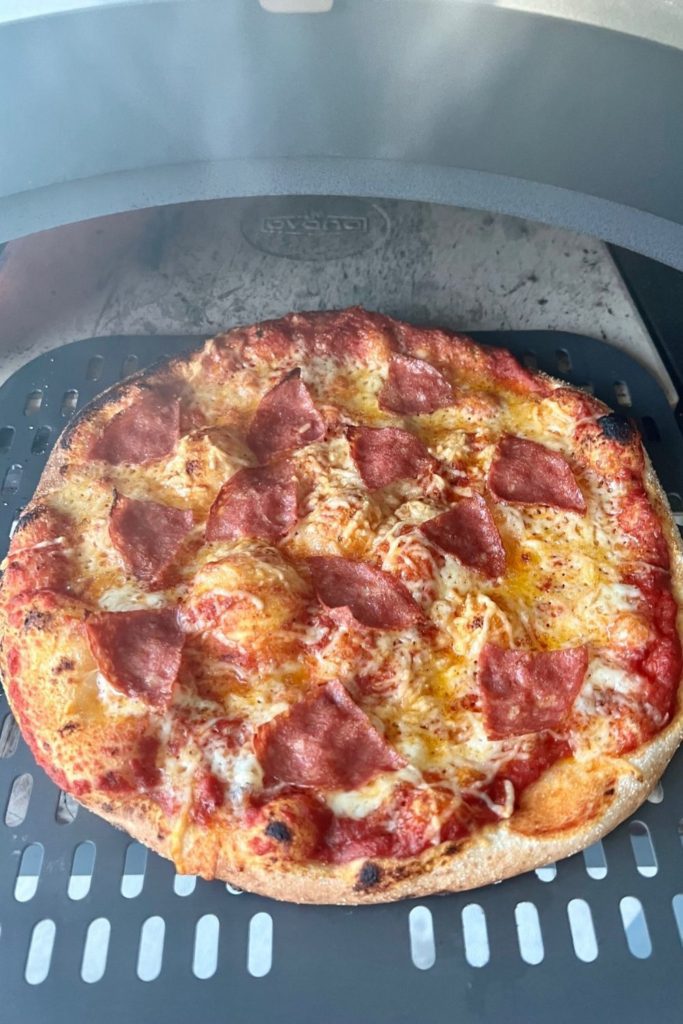 Pizza de masa fermentada sacada del horno de pizza a gas usando una pala de pizza perforada.