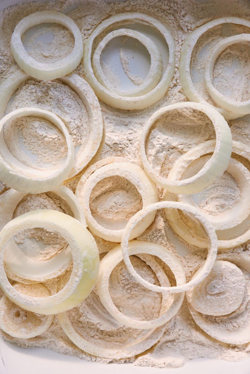 Una bandeja blanca de rebanadas de aro de cebolla recubiertas de harina