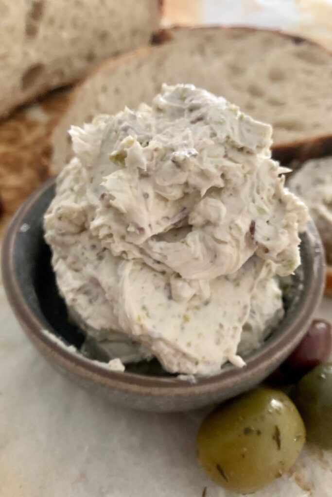 Tazón de queso crema de oliva para untar sentado frente a pan de masa fermentada.